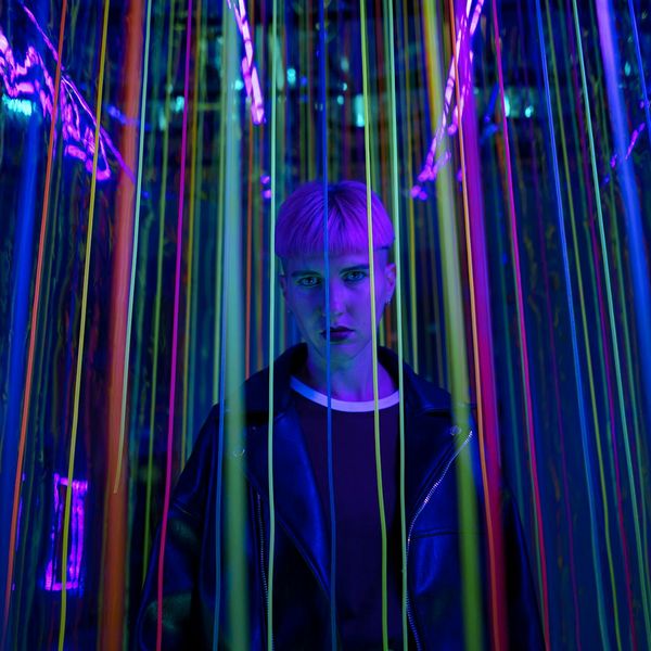 Man in a controlled balancing pose in a dark room with purple glow.